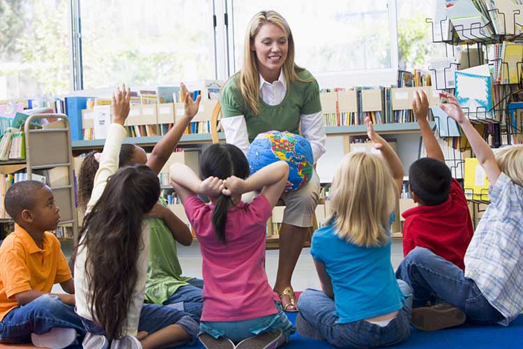 Kindergarten teacher and children with hands raised in library