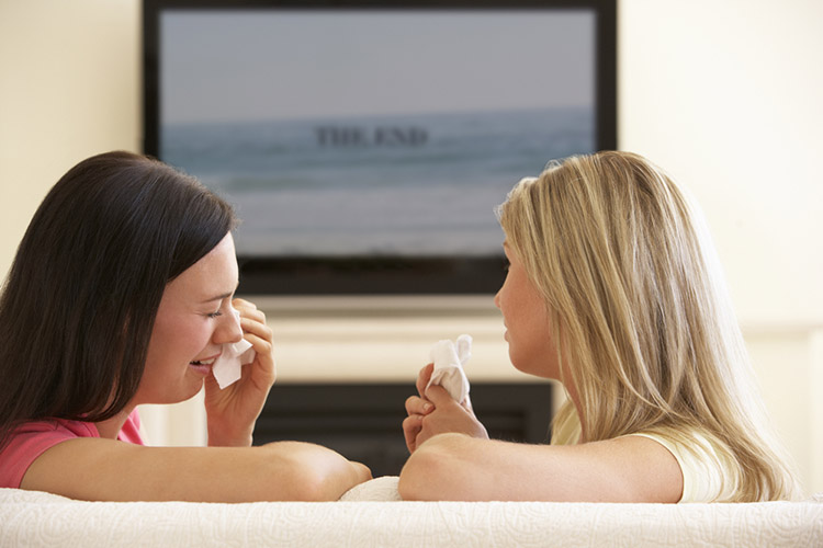 Two Women Watching Sad Movie On Widescreen TV At Home
